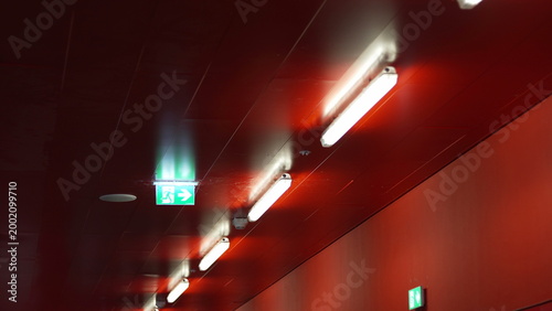 фотографія Fluorescent lights and green exit signs illuminating red corridor ceiling inside