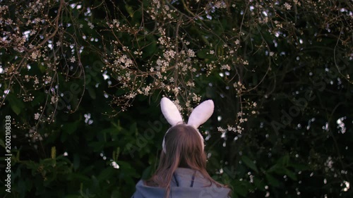 Woman wearing Easter bunny ears jumping by white cherry pink blossom tree flowers 