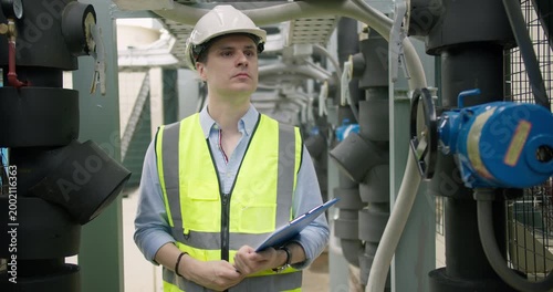A male engineer conducts a routine inspection of an industrial HVAC system in a plant room, checking machinery for performance and safety compliance.