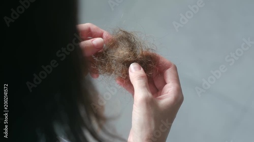 Over shoulder view, woman holding clump of fallen hair, showing signs of hair loss, damage, or alopecia, representing anxiety, stress, and health issues related to hair fall. 