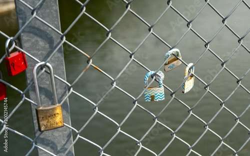 Colorful love locks attached to a chain-link fence overlooking water, symbolic romantic display with blurred background scenery.