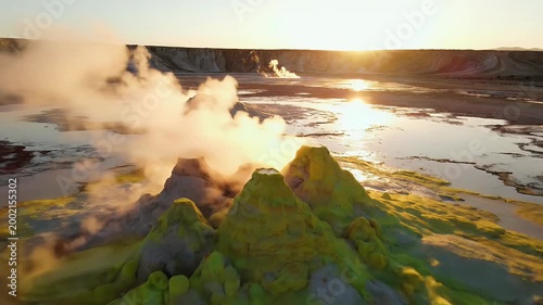 A stunning aerial view showcases a geothermal area with vibrant mineral deposits and steaming vents, bathed in the warm glow of the setting sun.