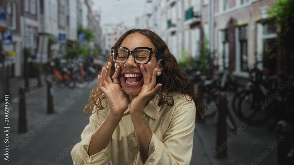 Fototapeta premium Woman with hands cupped around mouth and glasses on street lined with bicycles and narrow buildings; joyful playfulness.