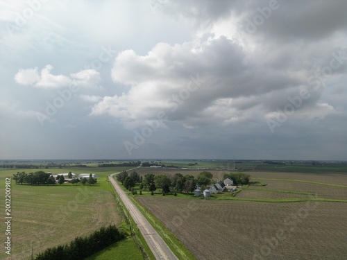 Darkening thunderstorm clouds (Cumulonimbus clouds) as you look down a country road in rural Illinois towards a farmstead. Long straight country roads.