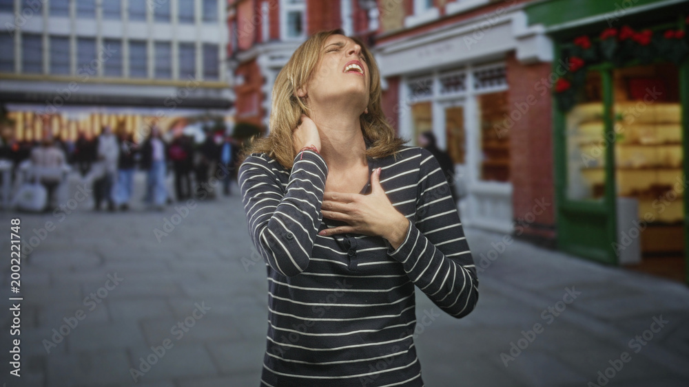 Fototapeta premium Woman clutching chest and pressing neck with hand in a busy urban shopping street by storefronts and crowds; pain urgency concern.