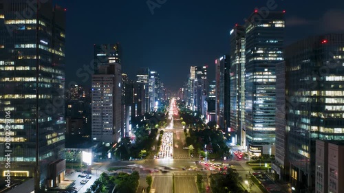Elevated time-lapse video of a modern city transforming from vibrant dusk to deep night, car light trails streak across multi-lane roads, thousands of windows illuminate, revealing an expansive