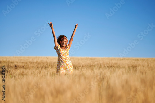 Happy woman raising arms in golden wheat field