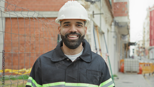 Bilde på lerret Man bearded wearing white hardhat and reflective vest smiling while standing at a street construction site as construction worker; pride duty