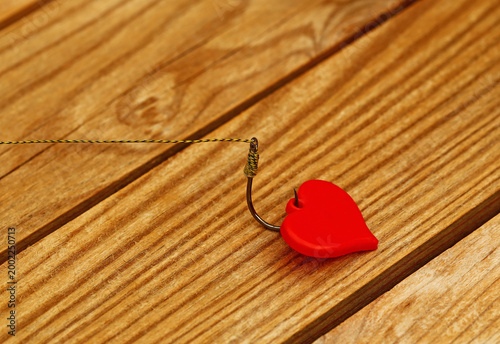 Fotografie Fishing hook with a red heart on wooden surface shows a mix of emotions and acti