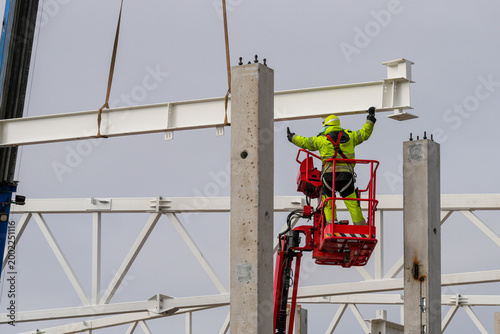Foto Construction worker guiding suspended steel beam into place on concrete columns