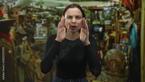 Canvas-taulu Woman with hands cupped to shout at a vintage diving helmet and crowded clothing racks in an indoor shop building; frustration
