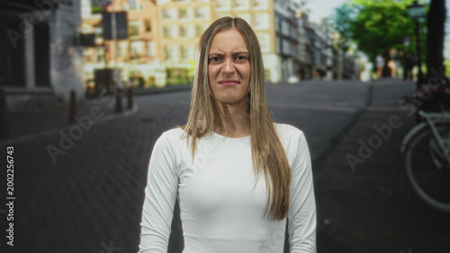 Photos Young hispanic woman grimaces with scrunched nose and pursed lips on a street, standing center frame; annoyance