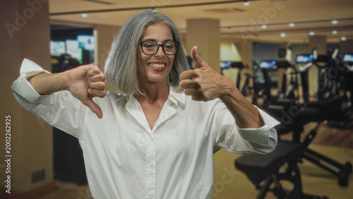 Foto Woman showing hands with one thumb up and one thumb down inside a gym building; ambivalence decision