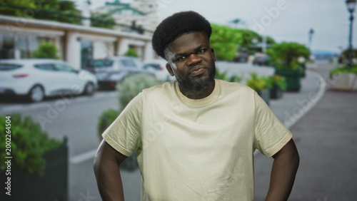 Canvastavla Man with hands on hips and frowning expression wearing beige tshirt on a city street; frustration defiance