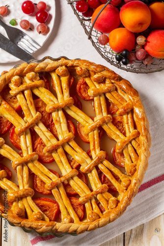 Apricot pie decorated with dough ornament and a metal basket with fruits and berries.