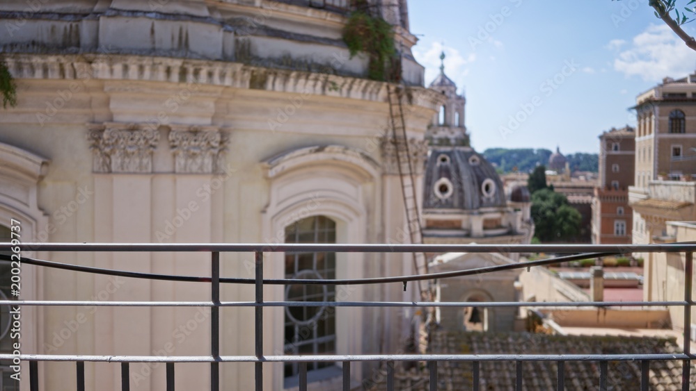 Fototapeta premium Balcony railing sharply focused with blurred domed rooftops and ornate building facades in soft bokeh city background; background backdrop copyspace calm.