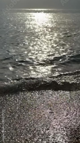 Ocean waves gently lapping at sandy beach under shimmering sunlight, creating peaceful background