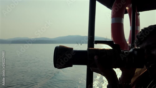 Person holding a camera on a boat while exploring a lake surrounded by mountains in the background during the day