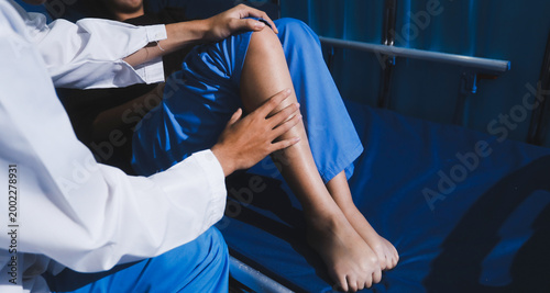 Bilde på lerret Asian male doctor examining foot of female patient sitting on bed in hospital room