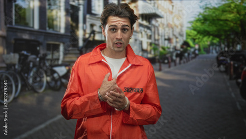 Foto Man in orange prison jumpsuit numbered 3825869 with hands clasped and downcast gaze on a city street; remorse reflection