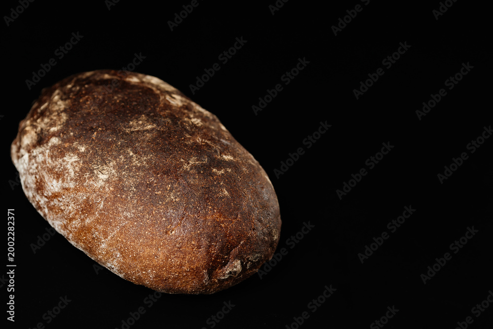 Naklejka premium Rustic sourdough loaf of artisan bread with deep crust on black background for bakery use