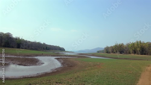 Hills and river under clear sky during daytime with green grass and distant trees in the background near the water