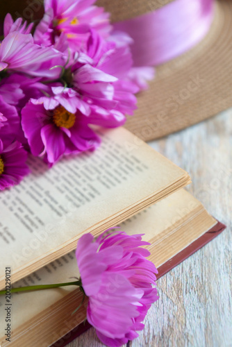 There are beautiful cosmos flowers, books and a hat on the table.