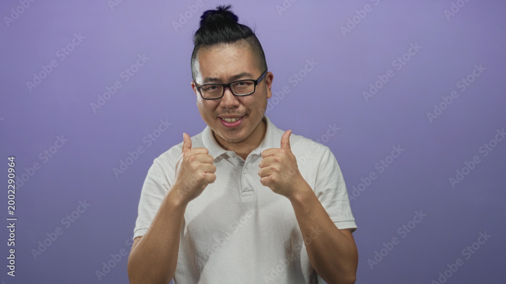 Obraz premium Young chinese man smiling and giving two thumbs up in purple studio wearing white polo shirt; positive approval.