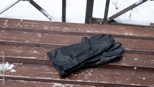 pair of black leather gloves on weathered wooden bench with snow. Winter accessory for cold weather protection and style.