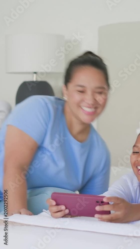 Vertical video: Reaching mom in pink picking phone, tapping gadget on bed, sharing clip with kids