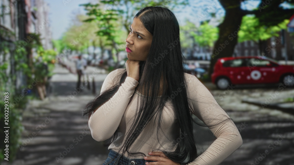Fototapeta premium Woman standing with hand on chin in pensive gesture on street amid parked cars; reflection introspection contemplation concern.