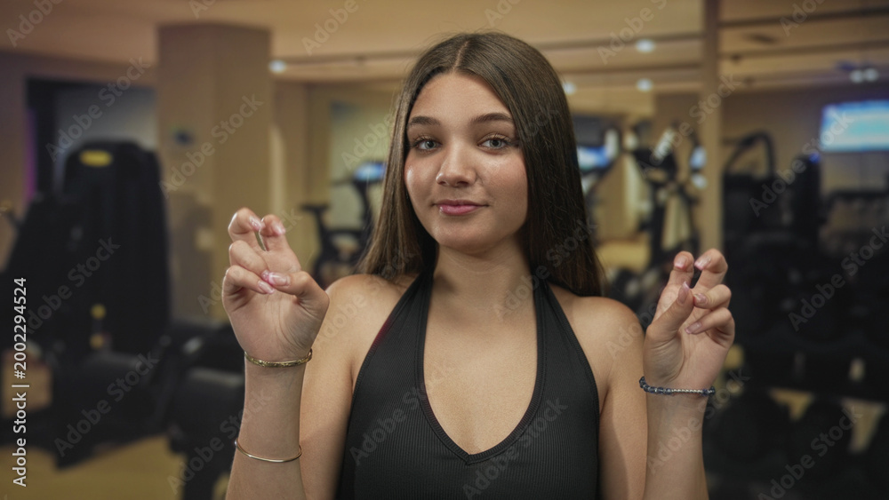 Naklejka premium Young woman shows clear airquotes with both hands in spacious brightly lit gymnasium area; sarcasm.