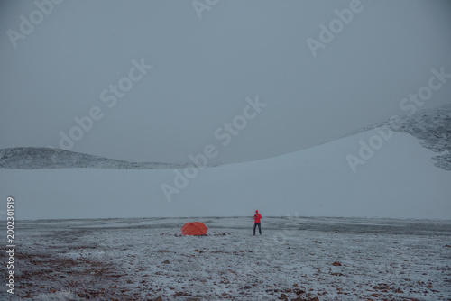 Man in red jacket in misty high mountains in freshly fallen snow. Orange tent...