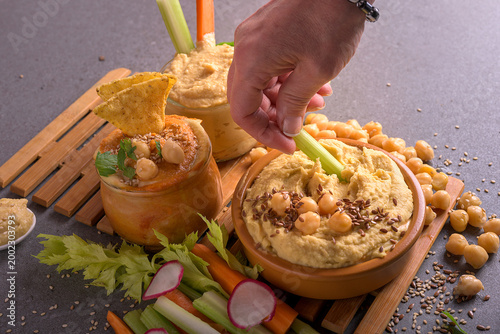 Fotografie Hand of a woman dipping a fresh vegetable stick into creamy hummus bowl with see