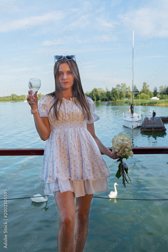 Obraz premium A joyful woman is celebrating by the peaceful water, holding vibrant flowers and enjoying the beautiful view around her