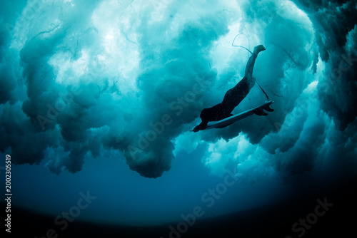 Surfer underwater beneath breaking wave in deep blue sea