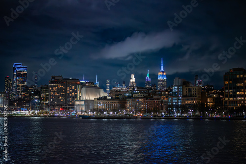 Stunning night time city scape of New York City Lower Manhattan from a cruise boat on the Hudson River under a stormy sky