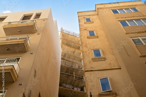 Canvas Print A low-angle view of a new multi-story residential building under construction with concrete floors and steel reinforcement, tightly squeezed between two existing apartment blocks