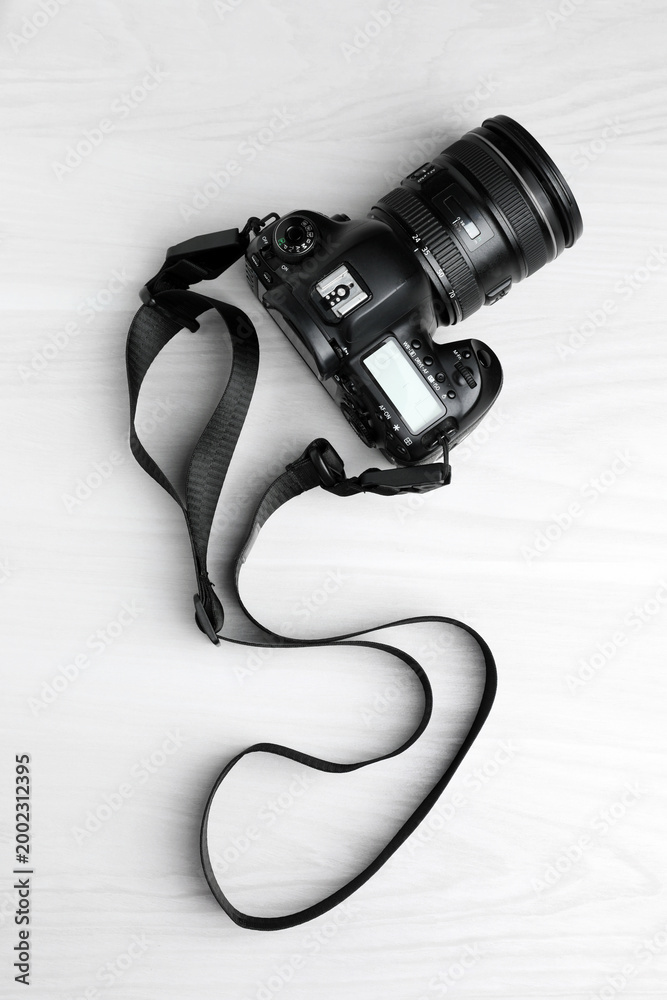 Naklejka premium Modern camera with strap on white wooden table, top view