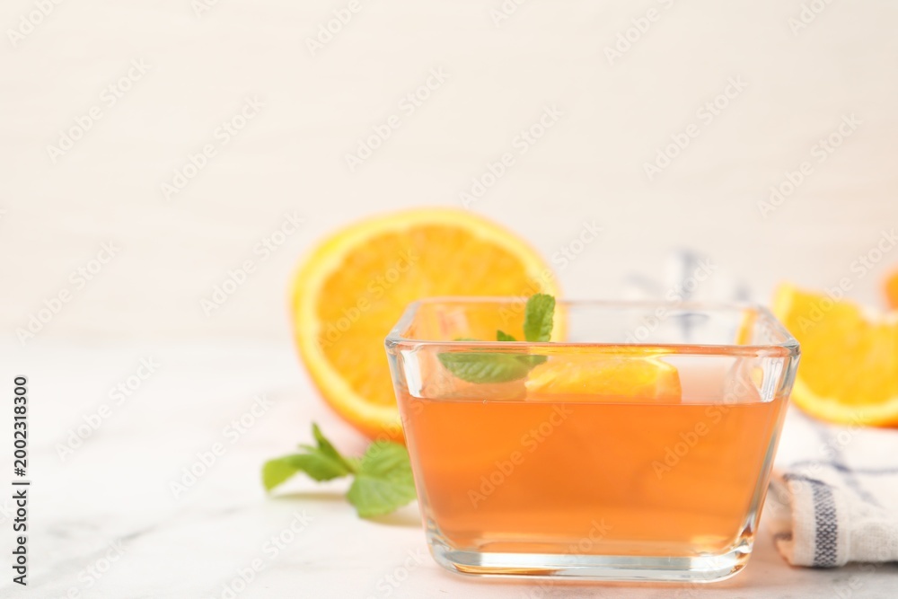 Fototapeta premium Yummy jelly in glass bowl, oranges and mint on white marble table, closeup. Space for text