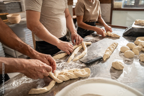 Bakers shaping braided dough at artisan bakery worktable