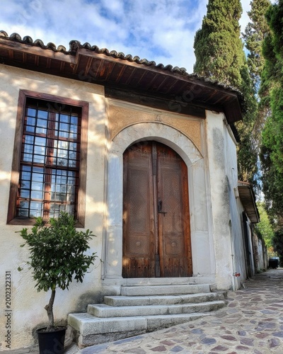 A historic building with wooden double doors under a decorative arch, and a window with a lattice pattern. Gray stone steps lead to the entrance.
