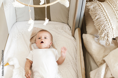 Adorable baby lying in crib with cute little toy and comforter. Time for sleep. Sweet infant portrait in boho bassinet top view. Childhood