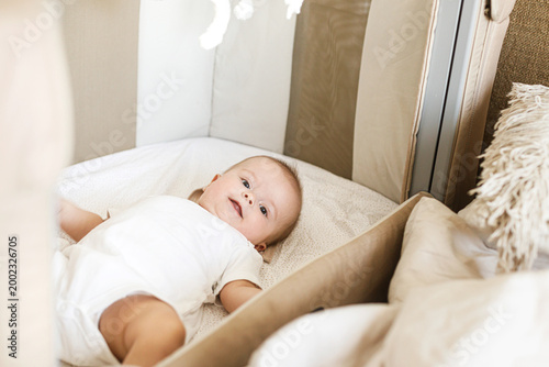 Adorable baby lying in crib with cute little toy and comforter. Time for sleep. Sweet infant portrait in boho bassinet top view. Childhood
