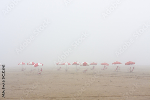 Foggy day at Santos beach with red umbrellas in a row