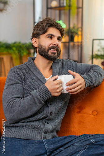 Fotografie Indian man at home holds hot tea or coffee warms hands looks out window gentle smile calm