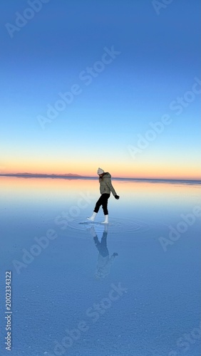 Φωτογραφία Woman standing on Salar de Uyuni salt flat at sunset with water reflection and o