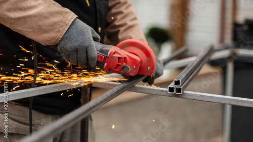 Metal worker uses a tool to cut steel while sparks fly at a construction site in the afternoon