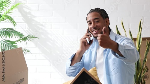 Smiling young afro-latino man at home with moving boxes, looking successful and okay