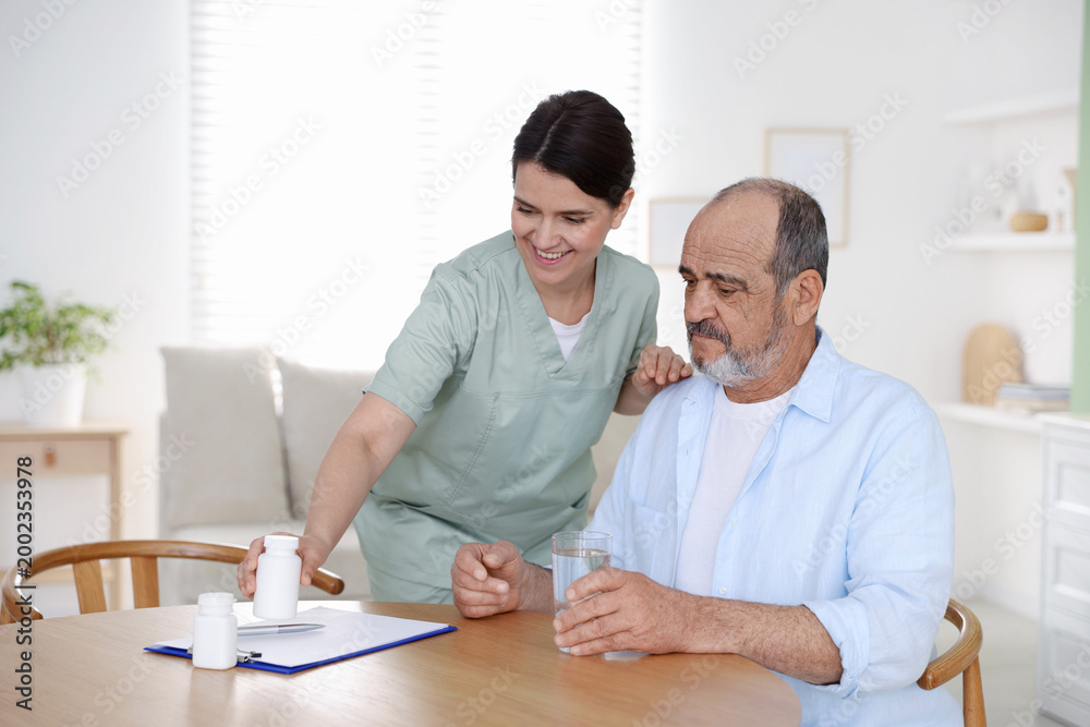 Obraz premium Smiling care worker working with senior man at wooden table at nursing home